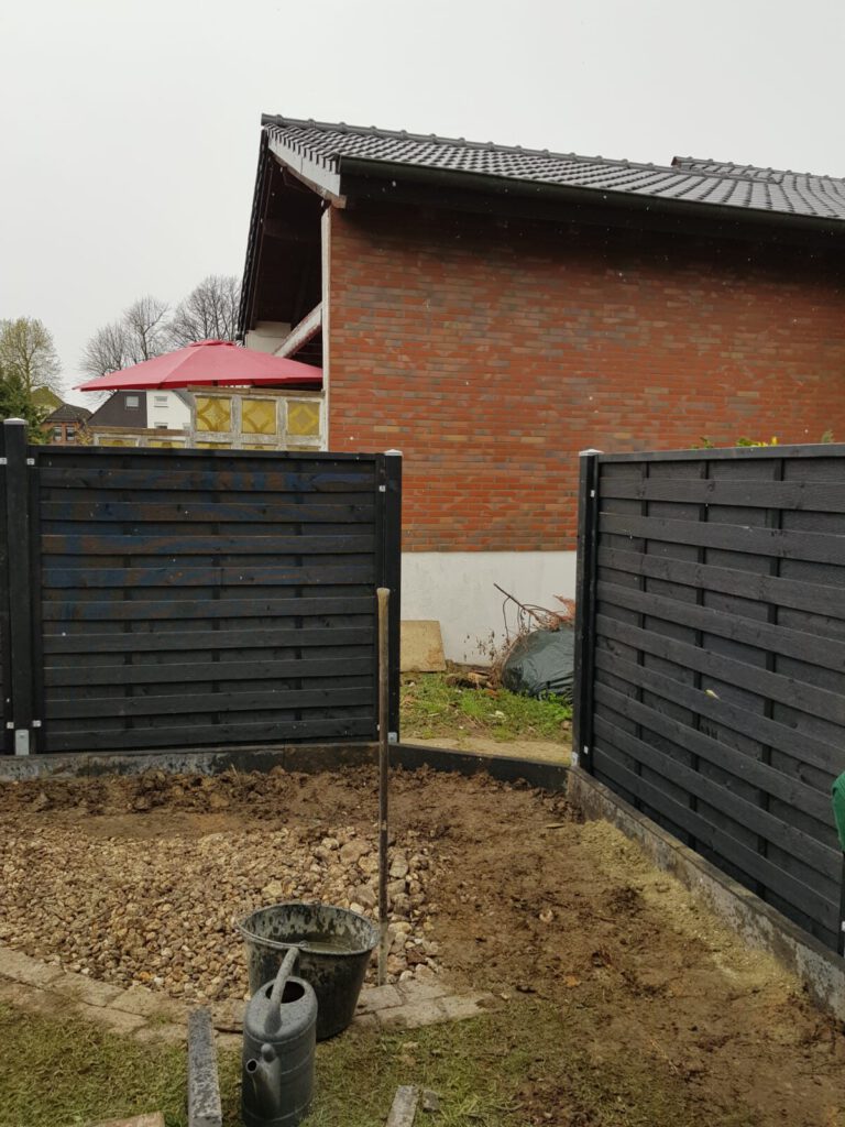 AT Garten- & Tiefbau Bauarbeiten im Garten mit einem Sichtschutzzaun und einem Pflanzgefäß im Vordergrund.