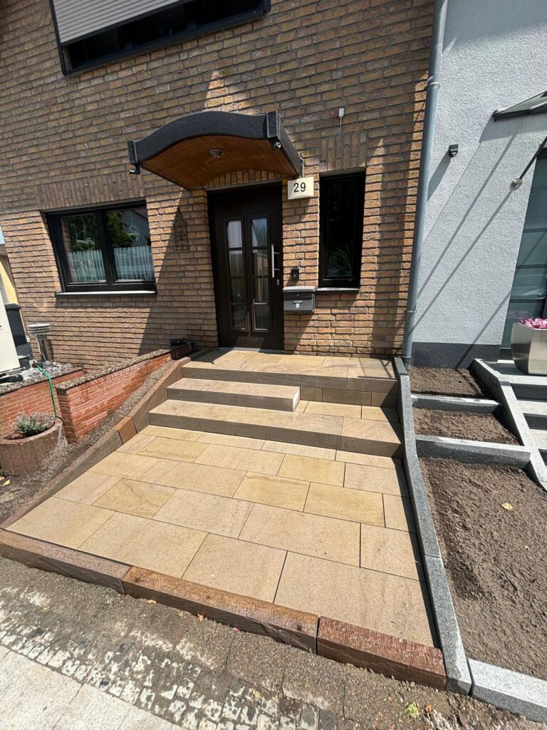 AT Garten- & Tiefbau Gepflasterter Eingangsbereich mit Treppe und Hausnummer 29 an der Wand.